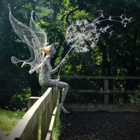 wire sculpture of fairy blowing a dandelion clock sitting on fence