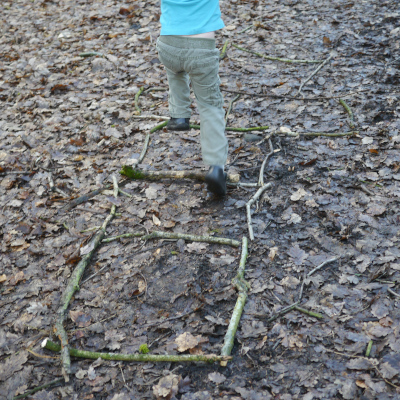 child playing hopscotch in woods using found sticks
