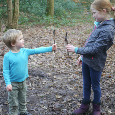 two children comparing sticks they have found in the woods