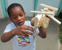 little boy holding up a handmade wooden helicopter