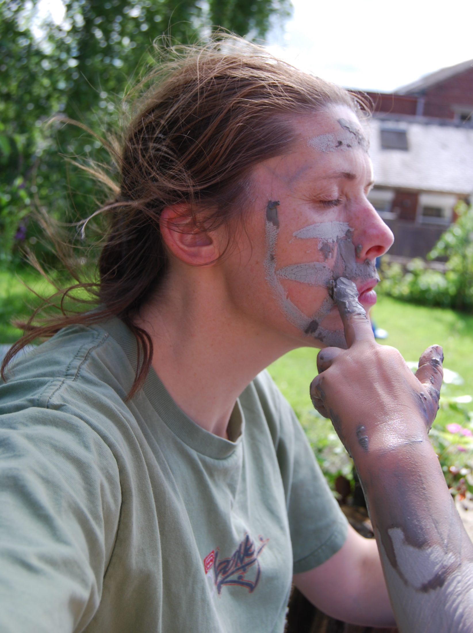 woman having her face painted in mud by a pair of small muddy hands