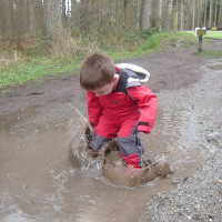 child jumping in a muddy puddle