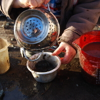 boy pouring mud through a sieve into a pot