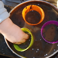 child putting a hand into muddy water and cup cake shells