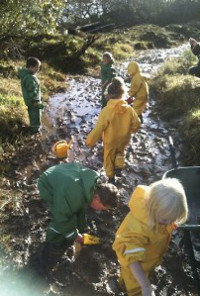 children in waterproofs paddling in a muddy stream