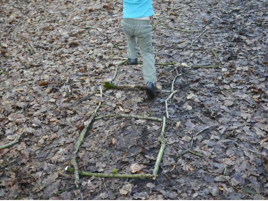 Child playing on a woodland hop skotch made with sticks.