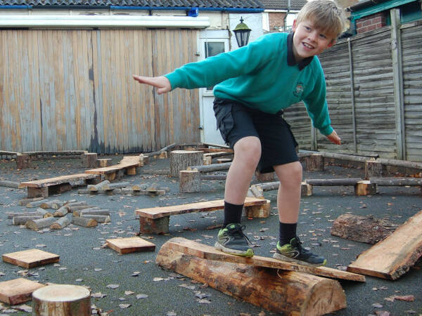 School aged child balancing on a plank on a rustic wooden obstacle course.