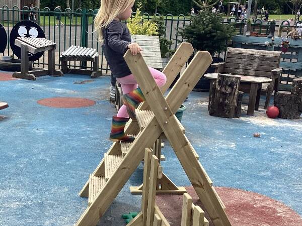 School aged child climbing over a free-standing stile in a school playground.