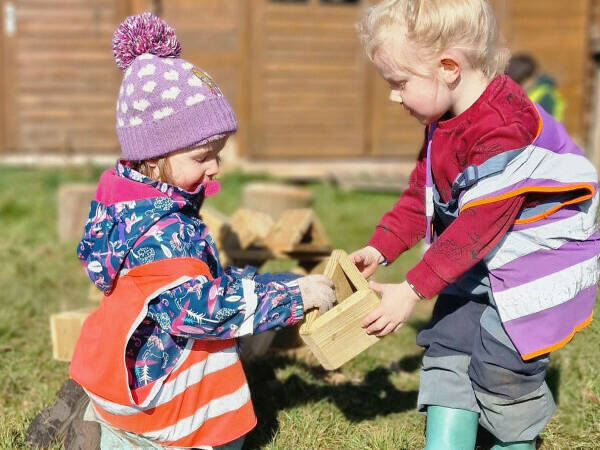 Nursery aged children engaged in block play lifting and carrying hollow wooden blocks.